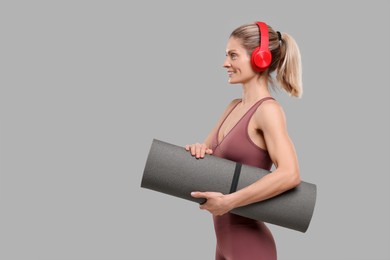 Photo of Sportswoman with headphones and fitness mat on grey background, space for text