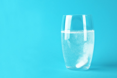 Photo of Glass of water with effervescent tablet on light blue background, space for text