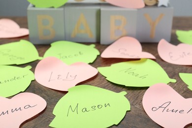 Photo of Paper stickers with different names on wooden table, closeup. Choosing baby's name