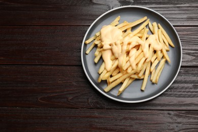 Photo of Delicious french fries with cheese sauce on wooden table, top view. Space for text
