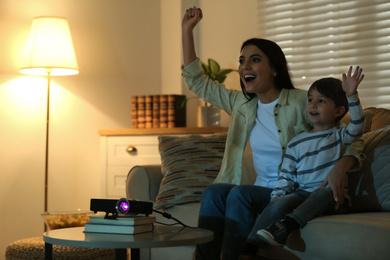Photo of Emotional young woman and her son watching TV using video projector at home. Space for text