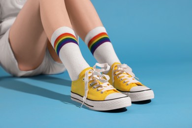 Photo of Woman wearing yellow classic old school sneakers on light blue background, closeup