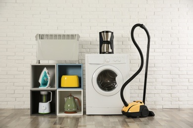 Photo of Modern vacuum cleaner and different household appliances near white brick wall indoors