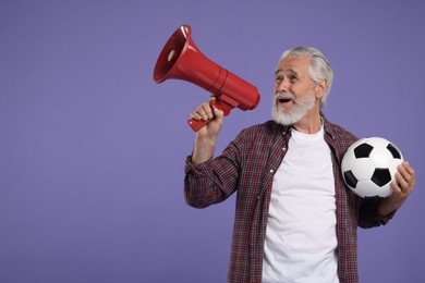 Photo of Emotional senior sports fan with soccer ball using megaphone on purple background, space for text