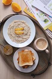 Photo of Wooden tray with delicious breakfast and magazines on table, flat lay
