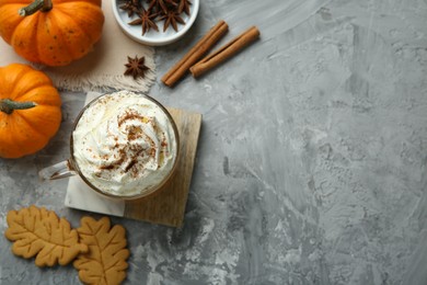 Photo of Cup of pumpkin spice latte with whipped cream, cookies and ingredients on light grey table, flat lay. Space for text