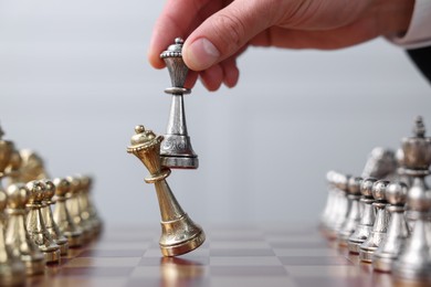Photo of Man with bishop game piece playing chess at checkerboard against grey background, closeup