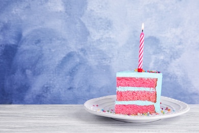Photo of Slice of fresh delicious birthday cake with candle on table against color background. Space for text