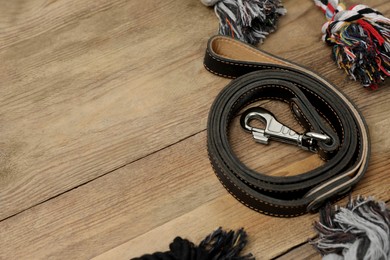 Photo of Black leather dog leash and toys on wooden background, space for text
