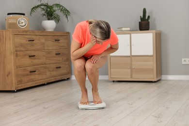 Photo of Surprised woman standing on floor scales at home