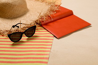 Striped beach towel, hat, book and sunglasses on sand, closeup