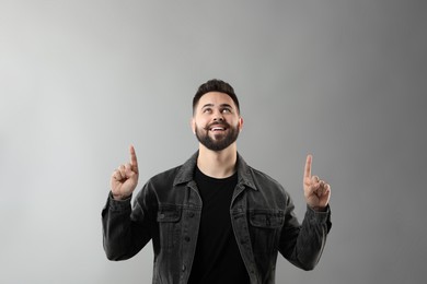 Young man with mustache pointing at something on grey background. Space for text