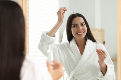 Photo of Beautiful woman applying hair serum indoors, reflection in mirror. Cosmetic product