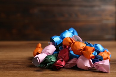 Photo of Many candies in colorful wrappers on wooden table. Space for text