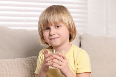 Photo of Cute little boy holding glass of fresh water indoors