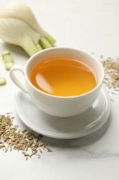 Photo of Fennel tea in cup, seeds and fresh vegetable on white marble table, closeup