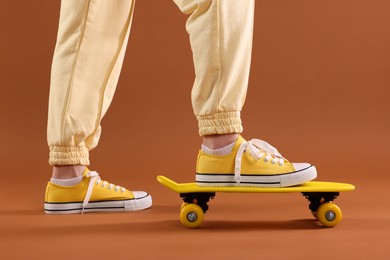 Photo of Woman in yellow classic old school sneakers standing on penny board against brown background, closeup