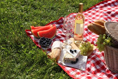 Photo of Picnic blanket with delicious food and wine outdoors on summer day, space for text