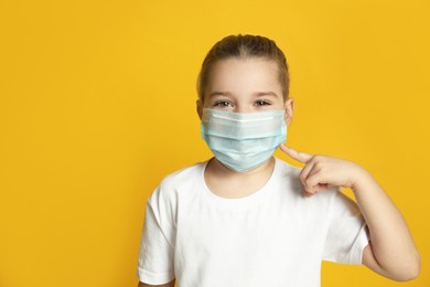 Photo of Cute little girl in protective mask on yellow background