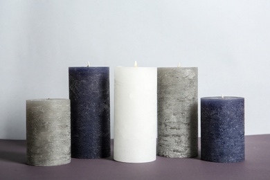 Photo of Different decorative wax candles on table against light background