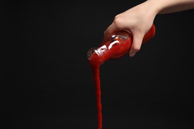 Photo of Woman pouring tasty ketchup from bottle on black background, closeup. Space for text