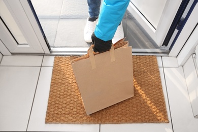 Photo of Courier bring paper bags with takeaway food to doorway, closeup. Delivery service during quarantine due Covid-19 outbreak