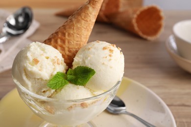 Photo of Delicious scoops of vanilla ice cream with wafer cone and mint in glass dessert bowl on table, closeup