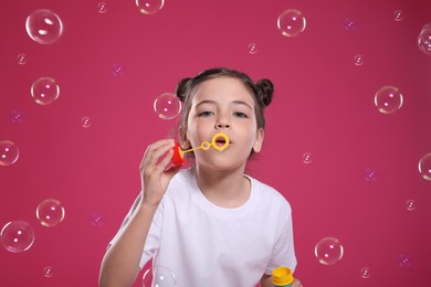Photo of Little girl blowing soap bubbles on pink background