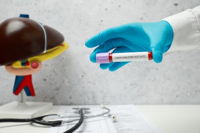 Photo of Laboratory worker holding tube with blood sample and label Liver Function Test over table, closeup. Space for text