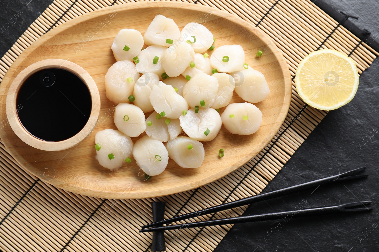 Photo of Raw scallops with green onion, soy sauce and lemon on dark textured table, flat lay