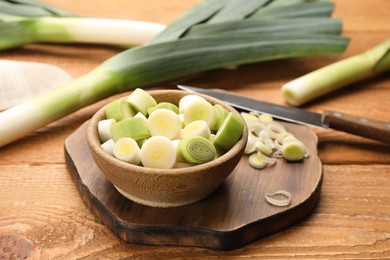 Photo of Fresh leek slices in bowl on wooden table, closeup