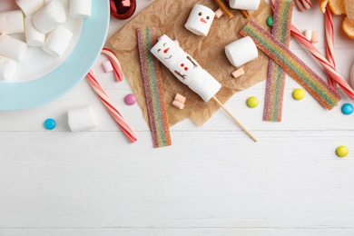 Photo of Flat lay composition with funny snowman made of marshmallows on white wooden table. Space for text