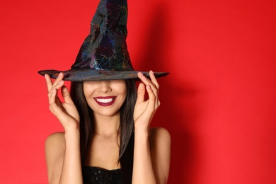 Photo of Beautiful young woman wearing witch costume for Halloween party on red background, space for text