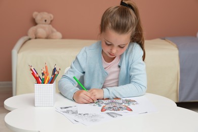 Photo of Little girl coloring antistress page at table indoors