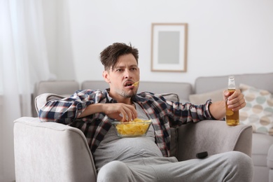 Photo of Lazy man with bottle of beer and chips watching TV at home