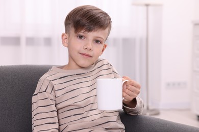 Photo of Cute boy with white ceramic mug on sofa at home