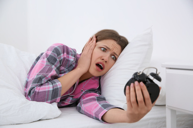Photo of Emotional young woman with alarm clock at home in morning