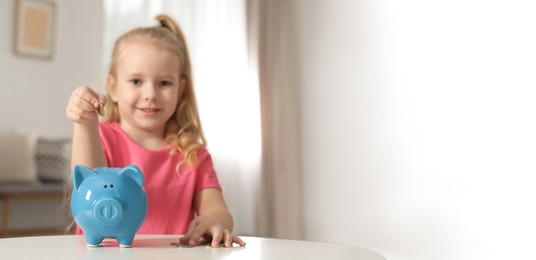 Cute girl putting coin into piggy bank at table in living room, space for text. Banner design