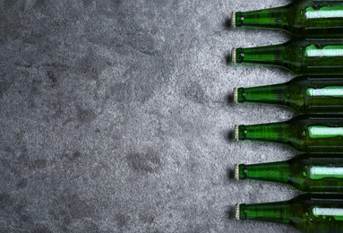 Photo of Green bottles with beer on grey table, flat lay. Space for text