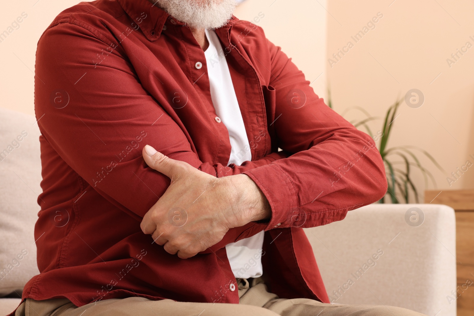 Photo of Senior man suffering from pain in his hand at home, closeup. Arthritis symptoms