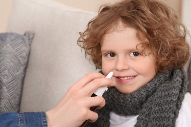 Photo of Mother using nasal spray to treat her little son on sofa, closeup