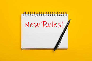 Image of Notebook with text NEW RULES and pen on yellow background, top view