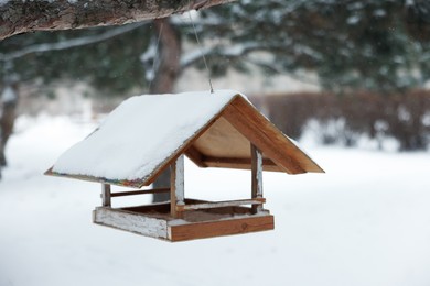Photo of Wooden bird feeder hanging outdoors on snowy day