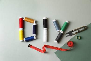 Photo of Abbreviation DIY made of spools of colorful threads and sewing supplies on color background, flat lay