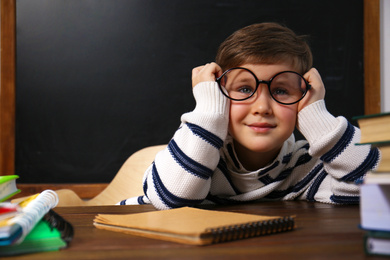 Photo of Cute little child wearing glasses at desk in classroom. First time at school