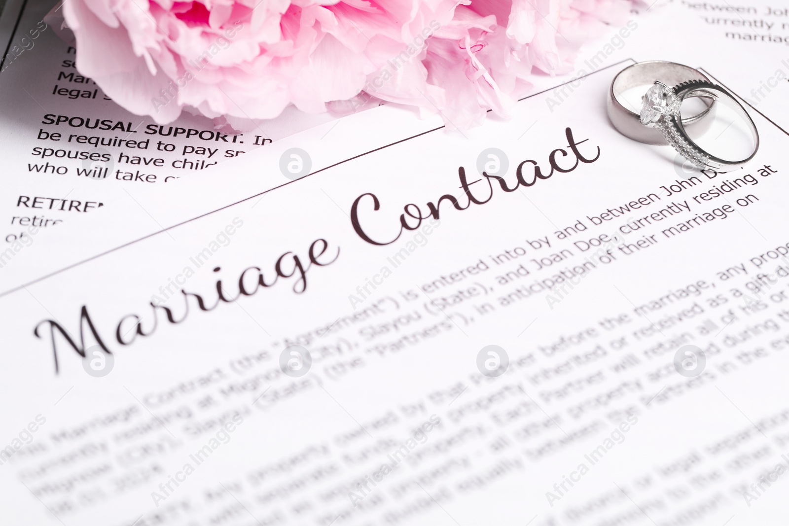 Photo of Marriage contract, wedding rings and flowers on table, closeup