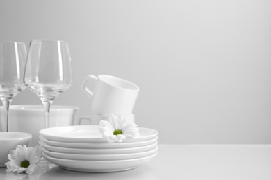 Photo of Set of many clean dishware, flowers and glasses on light table. Space for text