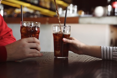 Photo of Couple with glasses of  cola at table indoors, closeup. Pouring refreshing beverage
