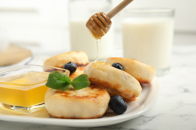 Photo of Pouring honey onto delicious cottage cheese on white marble table