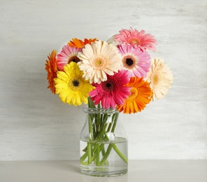 Photo of Bouquet of beautiful bright gerbera flowers in glass vase on table against wooden background